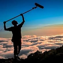 Person with Speaker Standing Next to Clouds During a Sunset